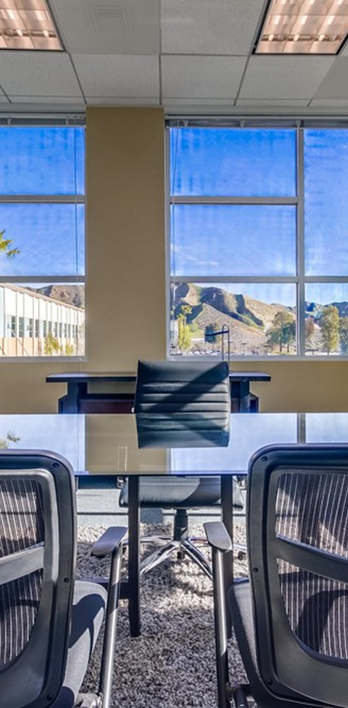 Barrister Suites Office Lease A modern office conference room with a glass table and black chairs, featuring large windows that show a bright blue sky and mountains outside.