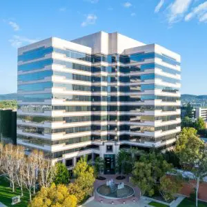 Barrister Suites Office Lease A modern, multi-story office building with reflective glass windows surrounded by trees, a circular driveway, and nearby buildings under a clear blue sky.