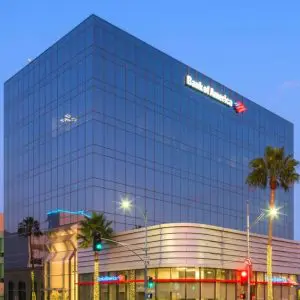 Barrister Suites Office Lease Glass office building with a Bank of America logo at the top, palm trees in front, and street lights and traffic signals at the intersection, photographed at dusk with a clear blue sky.