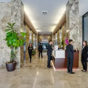 Barrister Suites Office Lease A modern office lobby with marble walls and floors, a large potted plant, and several people in business attire standing and talking near a reception desk.
