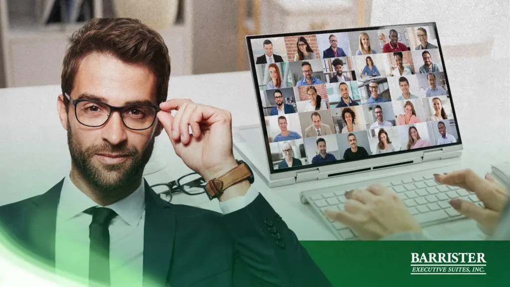 Barrister Suites Office Lease A confident man in glasses sits at a desk while a person types on a laptop displaying a video conference with many participants. The Barrister Executive Suites, Inc. logo appears in the bottom right corner.