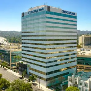 Barrister Suites Office Lease A tall office building with “Comerica Bank” signage at the top, surrounded by city streets, cars, trees, and other commercial buildings under a clear blue sky. Hills are visible in the background.
