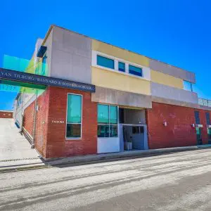 Barrister Suites Office Lease Modern two-story building with red brick and beige facade, large windows, and a sign reading Van Tilburg, Banvard & Soderbergh AIA. A driveway leads up to a parking area on the left, under a clear blue sky.