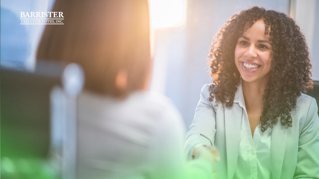 Barrister Suites Office Lease Two women in business attire are sitting across from each other and shaking hands in an office setting. One woman is smiling warmly. The Barrister Executive Suites, Inc. logo appears in the top left corner.