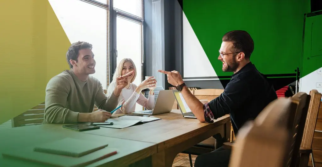 Barrister Suites Office Lease Three people sit at a wooden table in an office, smiling and talking, with laptops and notebooks in front of them. Colorful shapes overlay parts of the image, including green and yellow areas.