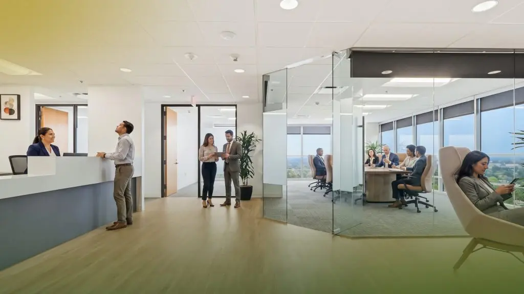 Barrister Suites Office Lease Modern office space with people interacting at a reception desk, two colleagues conversing in a hallway, a meeting taking place in a glass-walled conference room, and a person using a phone in a lounge chair near large windows.