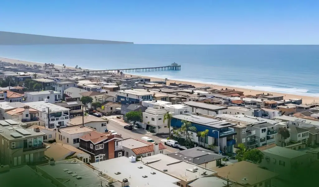 Barrister Suites Office Lease Aerial view of a coastal town with rows of houses, a sandy beach, and a long pier extending into the calm blue ocean under a clear sky.