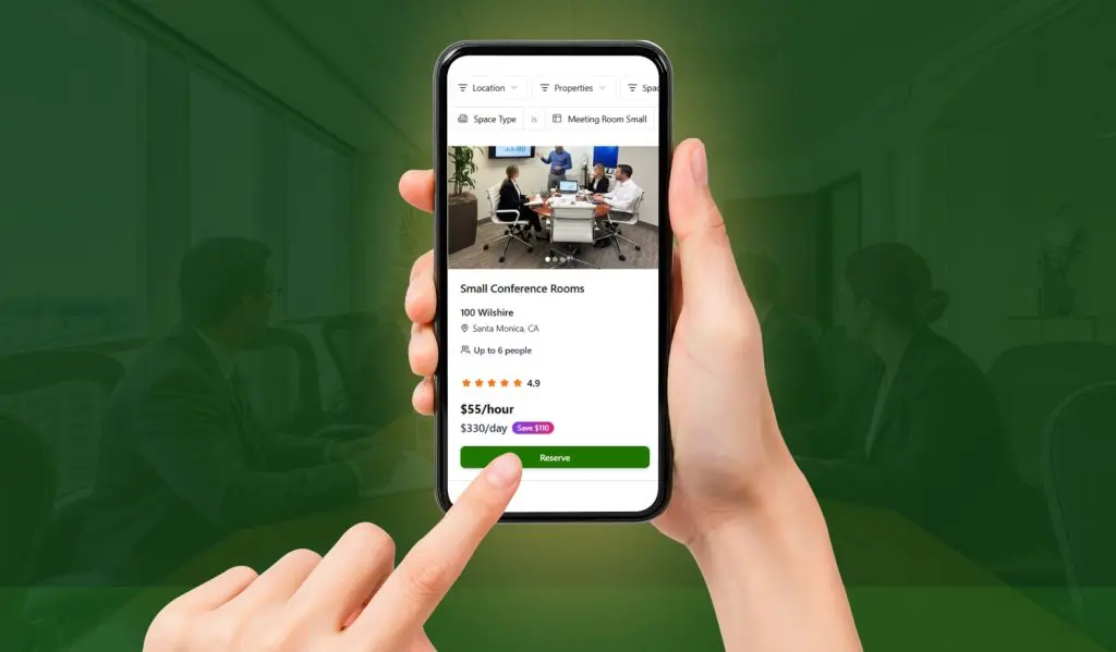 Barrister Suites Office Lease A hand holds a smartphone displaying a booking app for conference rooms, showing details and prices for a Small Conference Room. The background shows a blurred image of people meeting in a conference room.