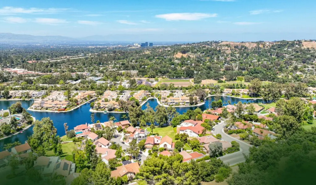 Barrister Suites Office Lease Aerial view of a suburban neighborhood with red-roofed houses, winding streets, lush greenery, and several small lakes, set against a backdrop of hills and distant city buildings under a clear blue sky.