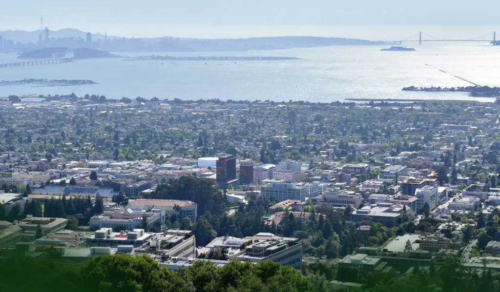 Barrister Suites Office Lease Aerial view of a city with numerous buildings and tree-lined streets, bordered by a large bay with bridges in the distance and a hazy skyline on the horizon.