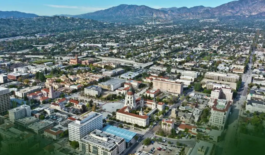 Barrister Suites Office Lease Aerial view of a city with many buildings, tree-lined streets, and distant mountains under a clear blue sky. The scene includes a mix of low-rise and mid-rise structures and busy roads running through the area.