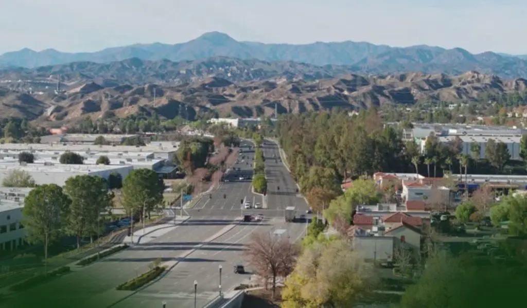 Barrister Suites Office Lease A wide street lined with trees runs through a city, with commercial buildings on both sides and rugged mountains in the background under a clear sky.
