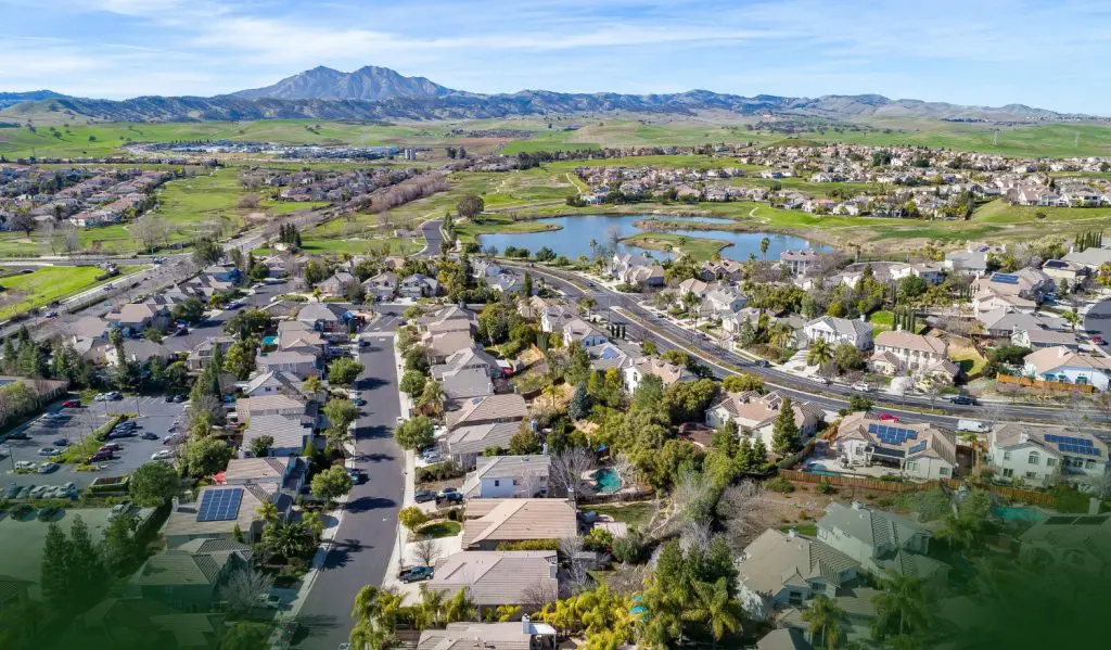 Barrister Suites Office Lease Aerial view of a suburban neighborhood with houses, roads, trees, and a small lake, set against rolling green hills and mountains under a blue sky.