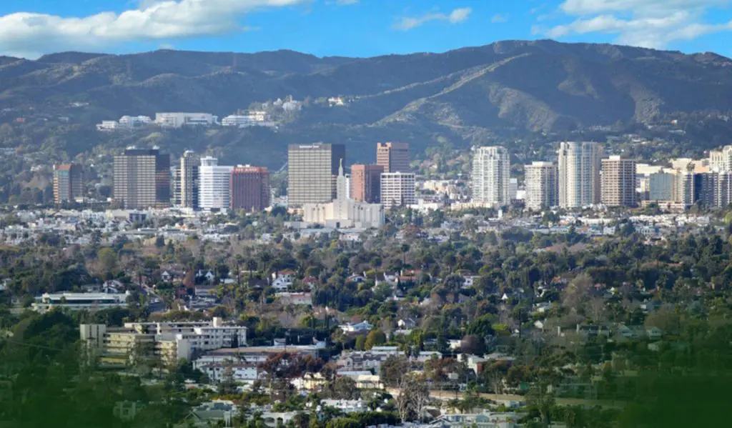 Barrister Suites Office Lease A cityscape with tall buildings and skyscrapers rises in the background, set against a backdrop of green hills and a partly cloudy blue sky. In the foreground are residential neighborhoods surrounded by trees.