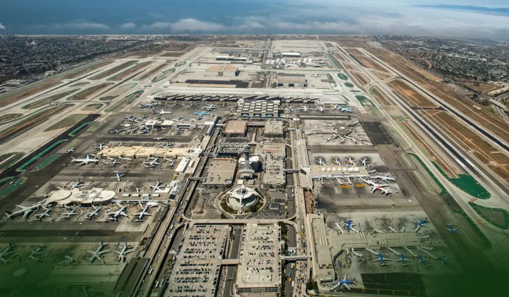 Barrister Suites Office Lease Aerial view of a large airport with multiple runways, taxiways, and terminal buildings; numerous airplanes are parked at gates, and the city and coastline are visible in the background.