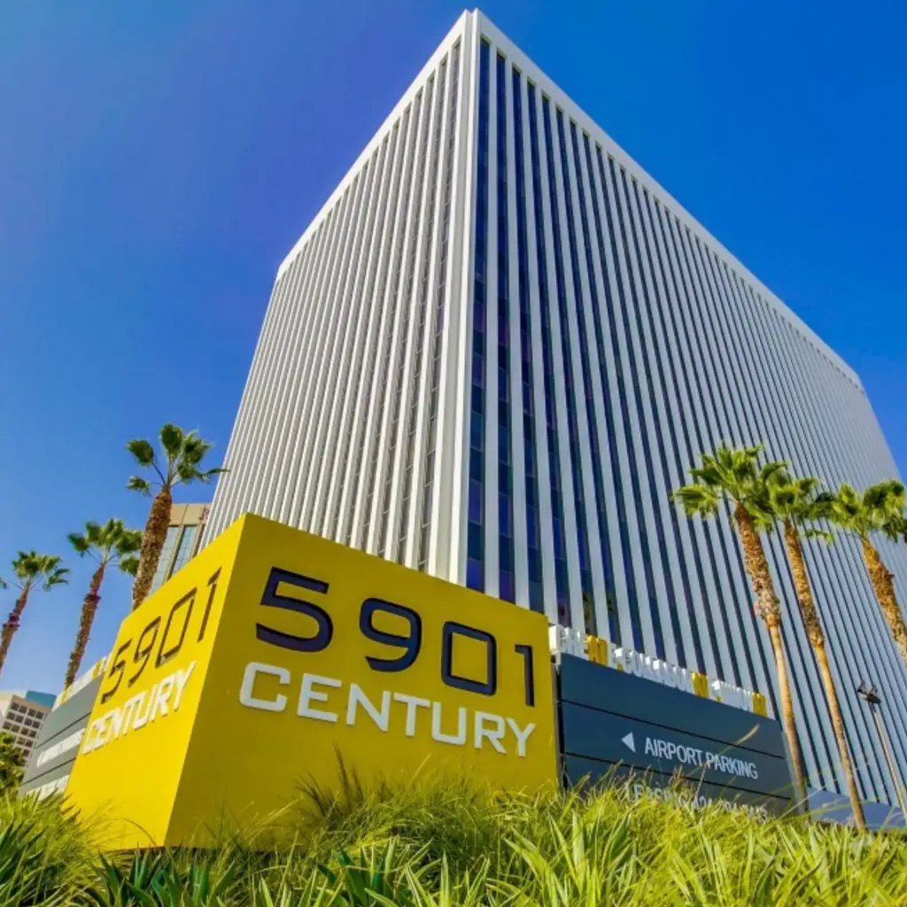 Barrister Suites Office Lease A tall office building with vertical lines stands behind a yellow sign that reads “5901 CENTURY.” Palm trees and clear blue sky frame the scene.