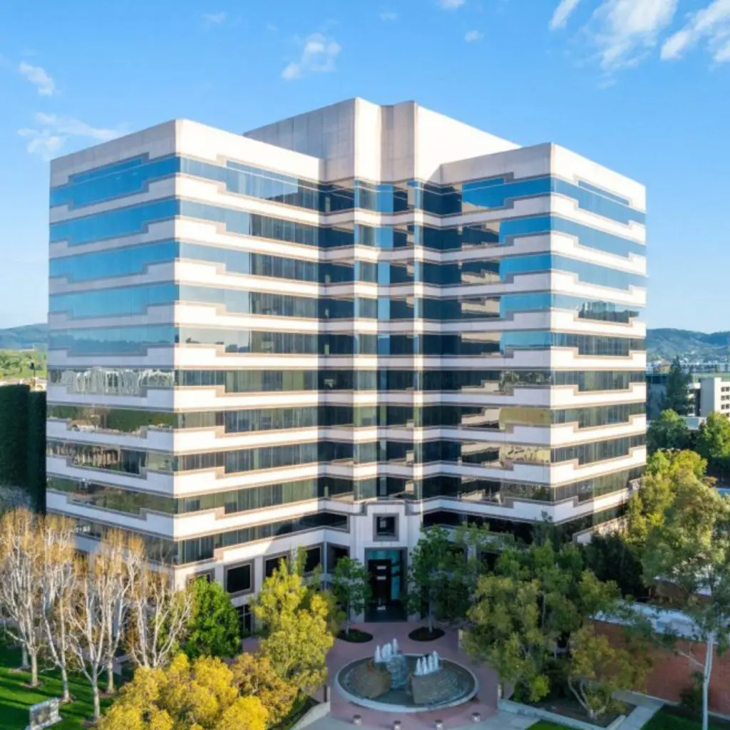Barrister Suites Office Lease A modern, multi-story office building with reflective glass windows, surrounded by green trees and landscaped grounds under a clear blue sky.
