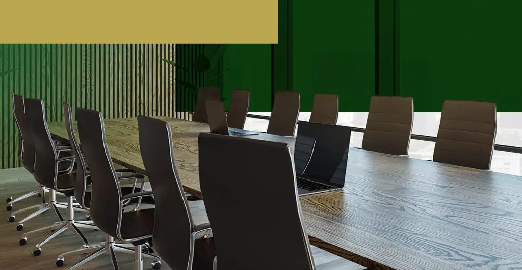 Barrister Suites Office Lease A modern conference room with a long wooden table, several black office chairs, a laptop on the table, and large windows with green shades in the background.