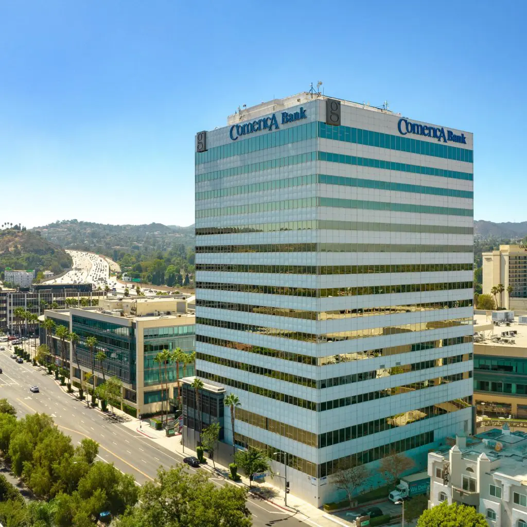Barrister Suites Office Lease A tall Comerica Bank office building with mirrored glass windows stands beside a busy street, surrounded by other commercial buildings and greenery under a clear blue sky.