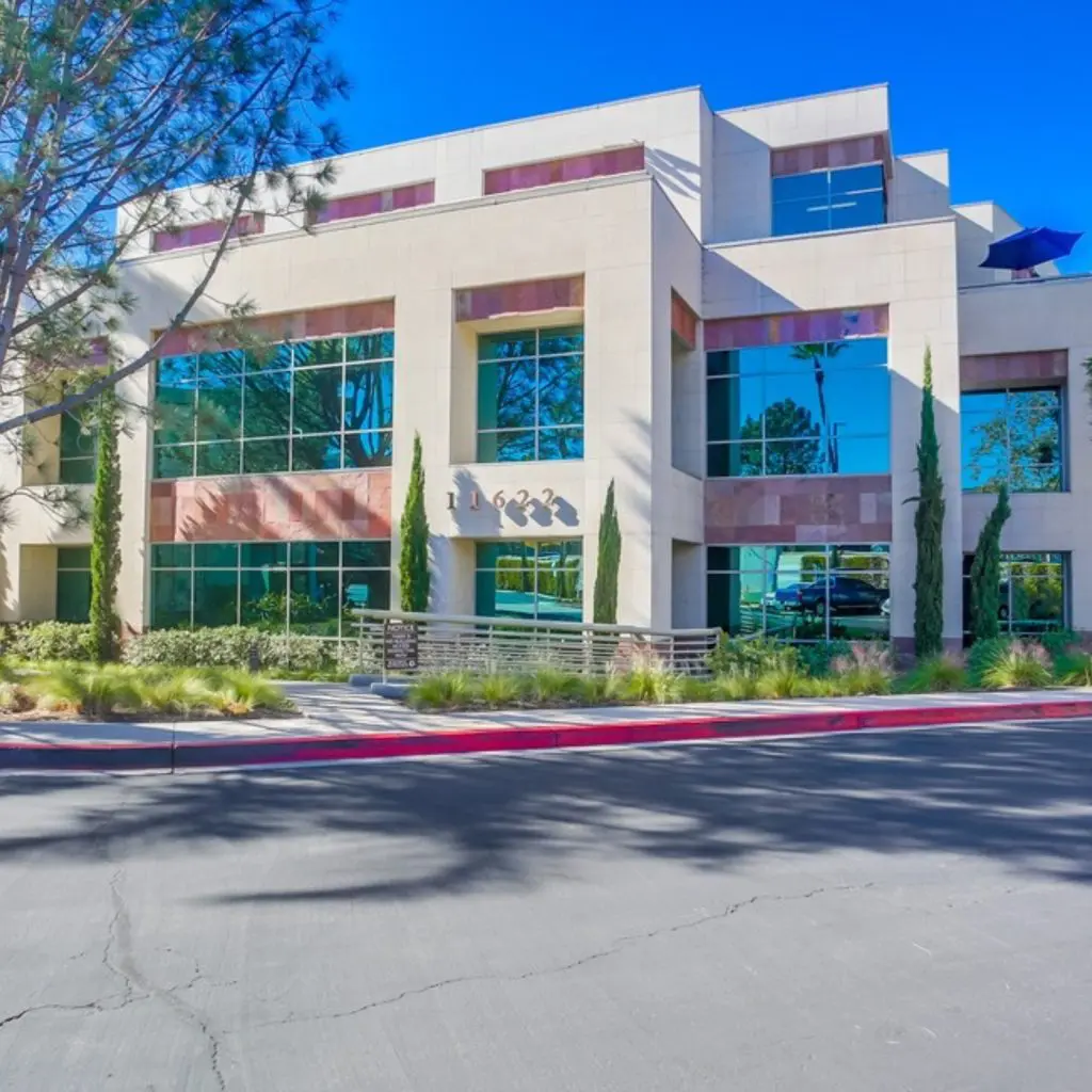 Barrister Suites Office Lease Modern three-story office building with large blue-tinted windows, surrounded by landscaped greenery and trees, under a clear blue sky. The address 11622 is displayed above the entrance.