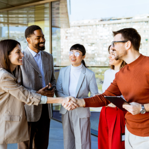 Barrister Suites Office Lease Five people in business attire stand together talking; two are smiling and shaking hands, while the others look on happily. The group is on a balcony with city buildings visible in the background.