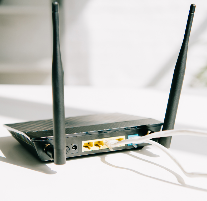 Barrister Suites Office Lease A close-up of a black Wi-Fi router with two antennas, standing on a white surface. Several network cables are plugged into the back ports of the device. Sunlight is shining on the router.