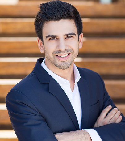Barrister Suites Office Lease A young man with dark hair, wearing a navy suit and white shirt, stands with arms crossed, smiling confidently. Wooden steps are blurred in the background.
