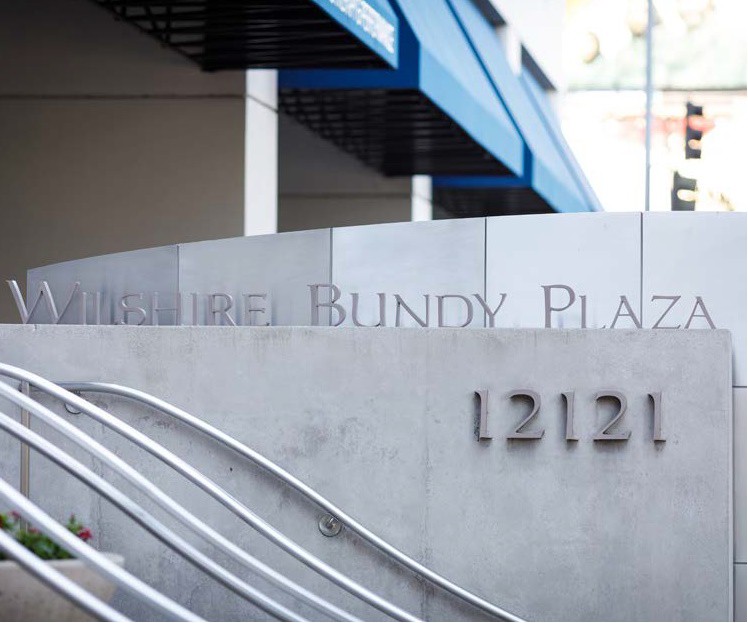 Barrister Suites Office Lease Modern building exterior with a sign that reads Wilshire Bundy Plaza and the street number 12121 on a concrete wall, with metal handrails and blue awnings visible.