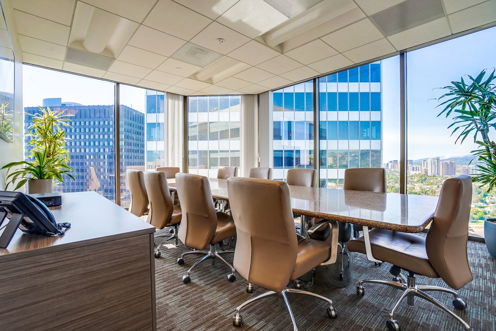 Barrister Suites Office Lease Modern conference room with a large marble table, beige chairs, floor-to-ceiling windows showing city buildings, potted plants, and sunlight streaming in, creating a bright and professional atmosphere.