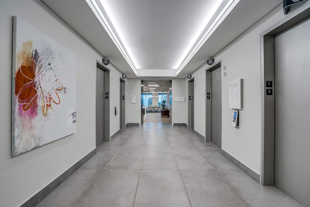 Barrister Suites Office Lease A modern, clean hallway with elevators on both sides, a large abstract painting on the left wall, and an office area visible through glass doors at the far end.