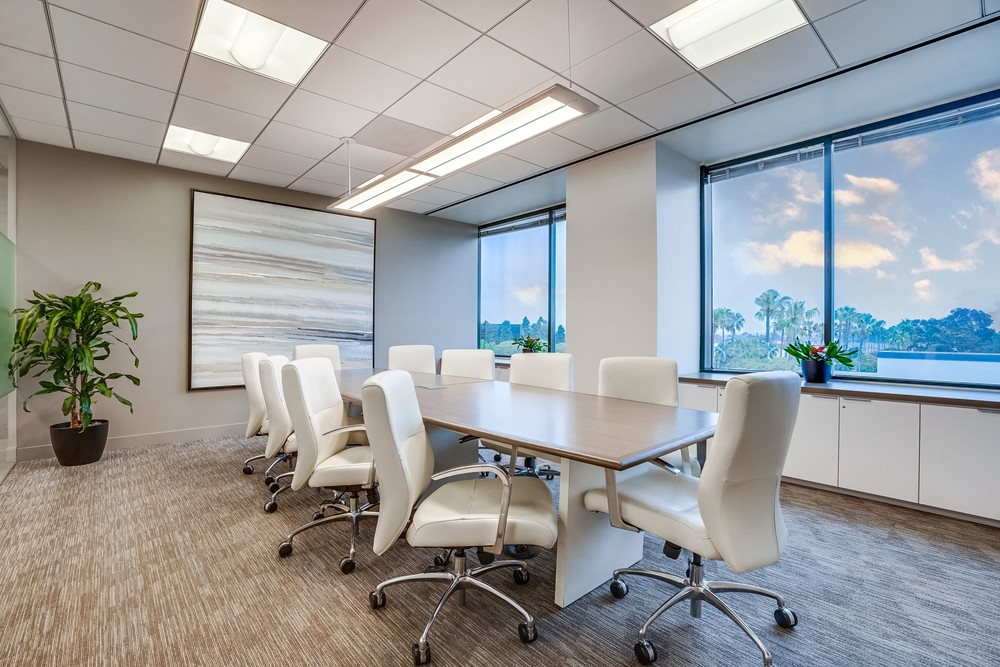 Barrister Suites Office Lease A modern conference room with a long wooden table surrounded by eight white office chairs, large windows with a view of trees and sky, and minimalist decor including plants and abstract wall art.