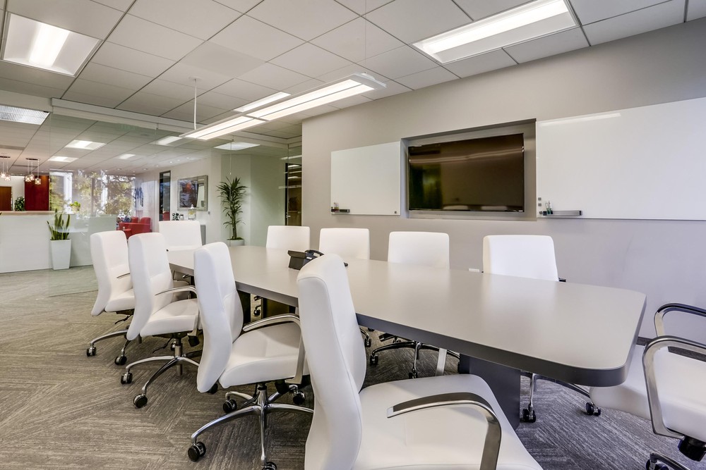 Barrister Suites Office Lease Modern conference room with a long gray table surrounded by white office chairs, two whiteboards on the wall, and large windows letting in natural light. The room appears clean and bright.