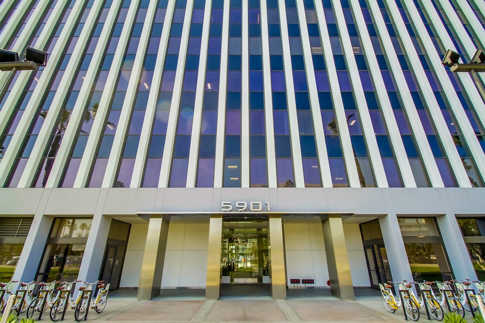 Barrister Suites Office Lease The image shows the entrance of a modern office building with the number 5901 above the doors. Several bicycles are parked at racks on both sides of the entrance. Tall vertical windows cover the buildings facade.
