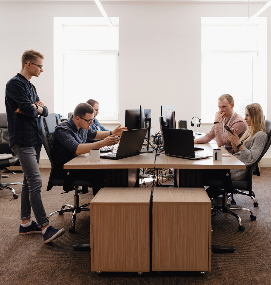 Barrister Suites Office Lease Five people are working collaboratively at desks with computers in a modern office, discussing and looking at screens. The atmosphere appears focused and engaged. Natural light streams in through large windows.