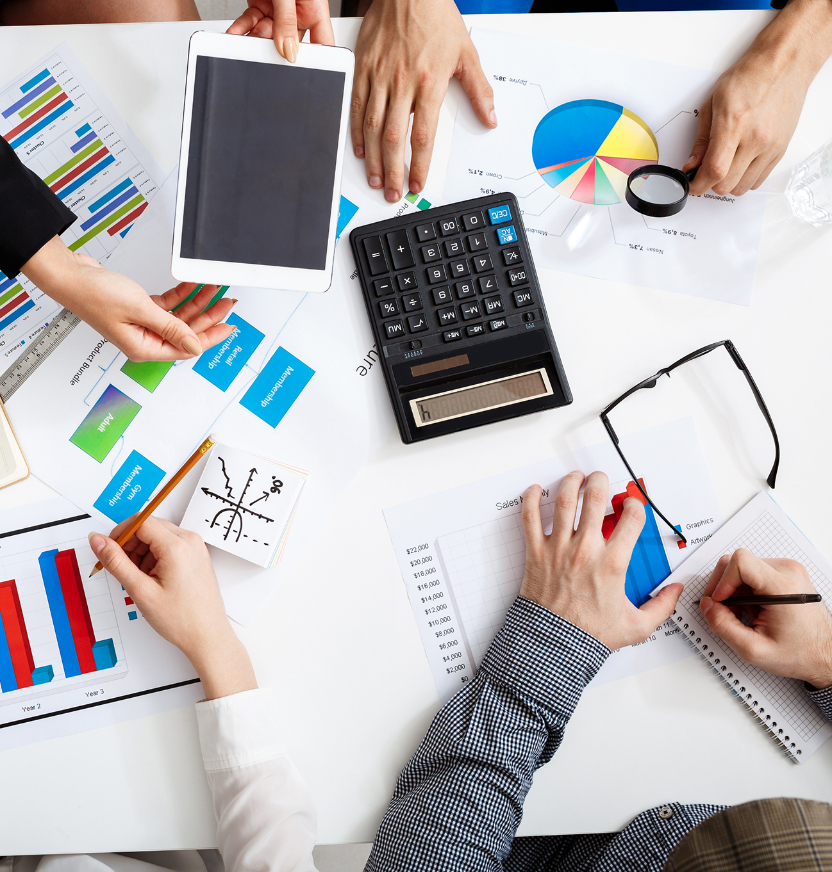 Barrister Suites Office Lease Four people work at a desk covered with charts, graphs, a calculator, a tablet, and papers; they analyze financial data and take notes during a collaborative business meeting.