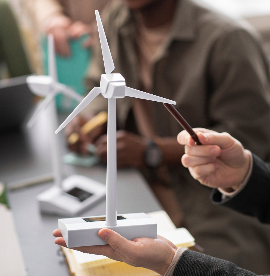 Barrister Suites Office Lease A close-up of hands holding a small wind turbine model in a classroom or office setting, with another model and two people blurred in the background.