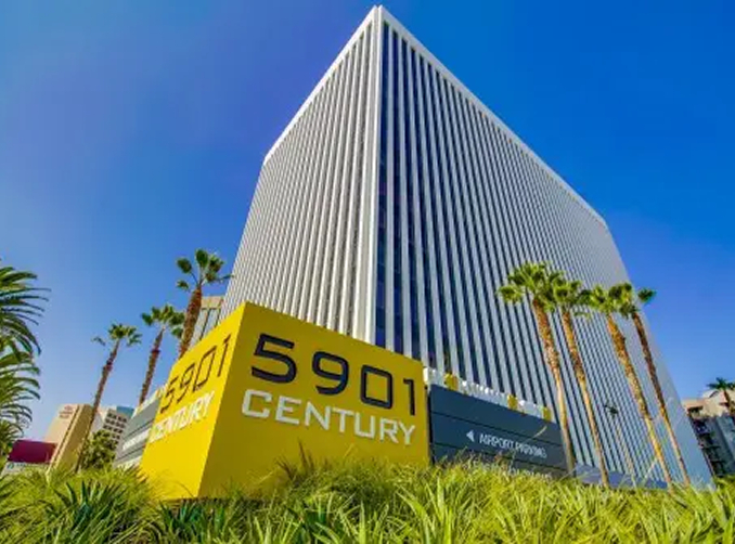 Barrister Suites Office Lease A tall, modern office building with vertical windows stands behind a yellow sign that reads 5901 CENTURY. Palm trees and greenery are in the foreground under a clear blue sky.