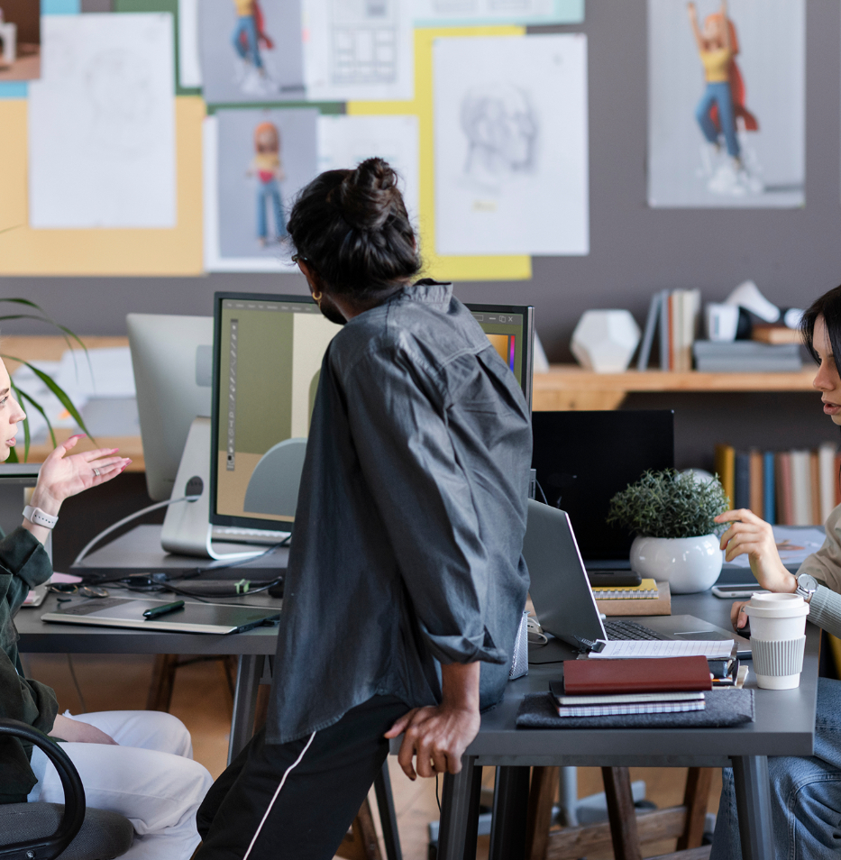Barrister Suites Office Lease Three people collaborate at a desk with computers, notebooks, and coffee cups in a modern office. Artworks and sketches are pinned to the wall behind them, creating a creative workspace atmosphere.