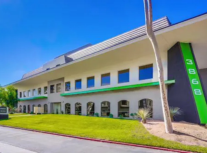 Barrister Suites Office Lease Modern two-story building with large windows, a green stripe along the facade, and the number 3868 displayed vertically on a dark pillar. There is a well-kept lawn and a clear blue sky.