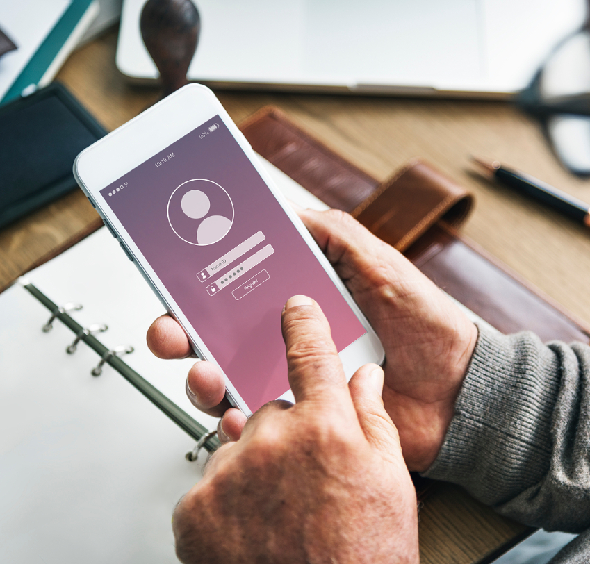 Barrister Suites Office Lease A person holds a smartphone, logging into an account with a username and password on the screen. An open notebook and a brown wallet are on the wooden desk in the background.