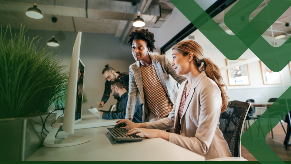 Barrister Suites Office Lease Two women in business attire work together at a computer in a modern office, with two other coworkers in the background. Green graphic overlays partially cover the image.