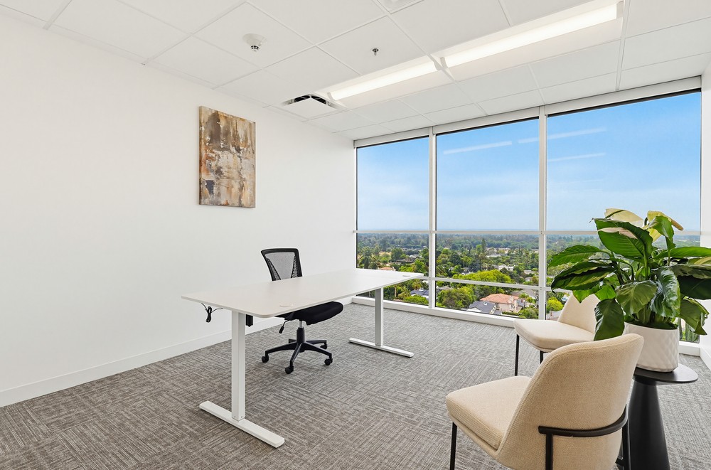 Barrister Suites Office Lease A modern office with a large window offering a scenic view, a white desk with a black chair, two beige guest chairs, a green potted plant, and abstract wall art. The room is bright, minimalist, and clean.