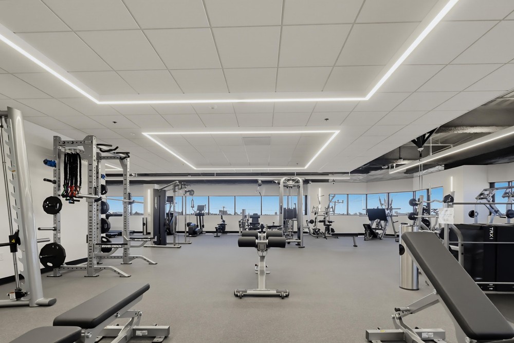 Barrister Suites Office Lease Modern gym with various exercise machines and equipment, including weight racks, benches, and cable machines, in a spacious room with large windows and bright overhead lighting.