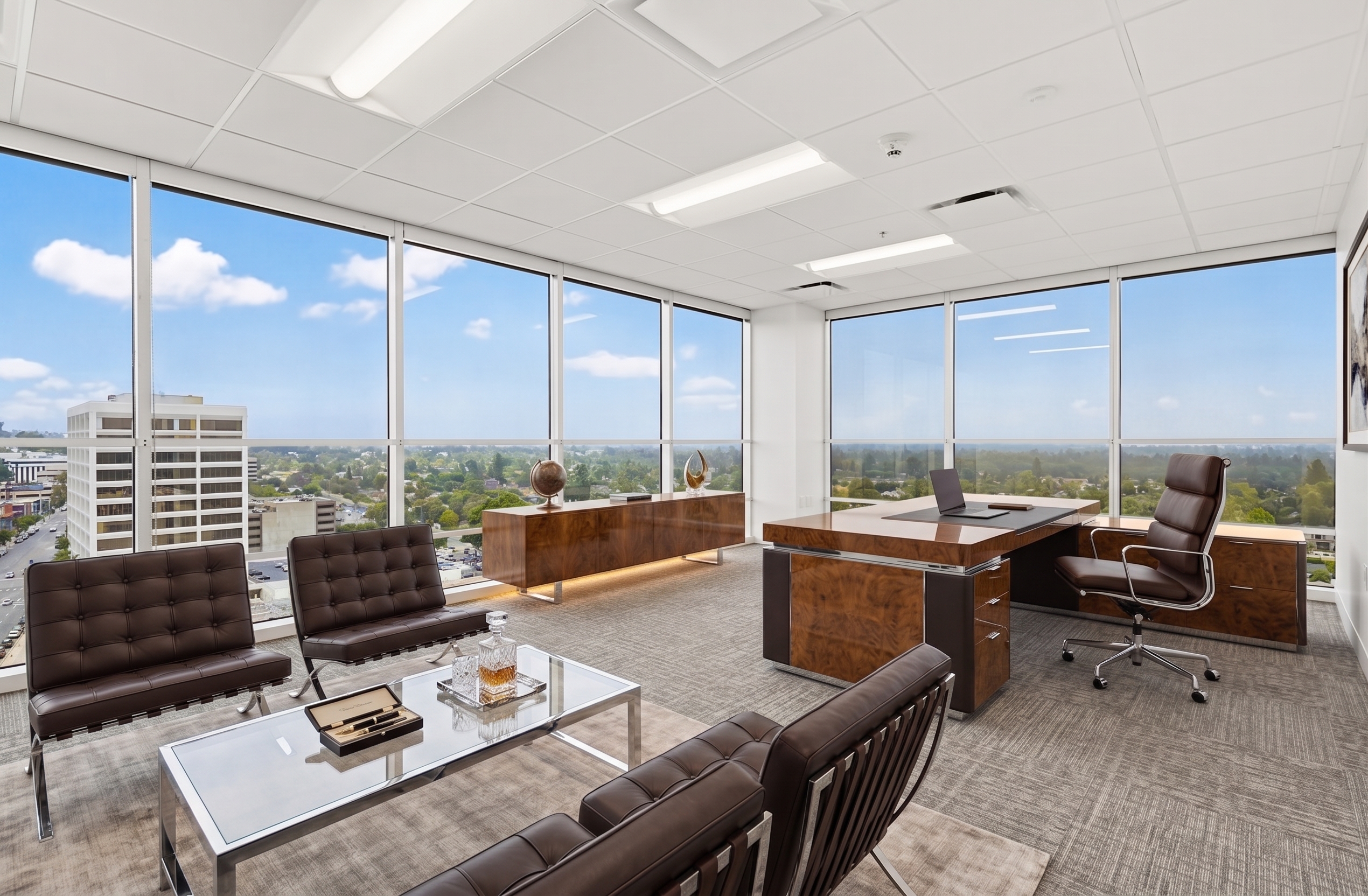 Barrister Suites Office Lease Modern office with large windows, brown leather chairs, glass coffee table, and a wooden desk with a computer. Cityscape and blue sky visible outside. Neutral colors and minimalist décor create a clean, professional atmosphere.