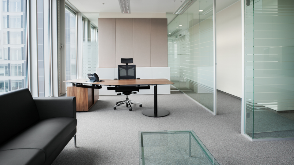 Barrister Suites Office Lease Modern office with a large desk, office chair, laptop, black sofa, and glass coffee table. Floor-to-ceiling windows and glass walls provide natural light and a spacious, minimalist atmosphere.