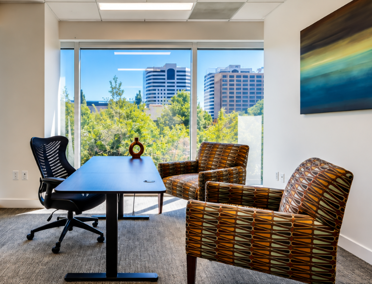 Barrister Suites Office Lease Modern office with a black desk, ergonomic chair, two patterned armchairs, abstract wall art, and large windows showing trees and city buildings in the background.