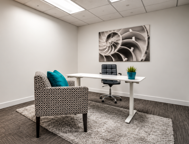 Barrister Suites Office Lease Modern office with a white desk, black chair, patterned armchair with blue pillows, small plant, and abstract shell artwork on the wall. Neutral colors and clean, minimal decor.